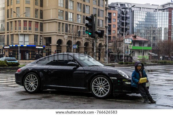 A poor boy begging while leaning against a\
expensive car showing divide between rich and poor in one city.\
Skopje, Macedonia 01.12.2017