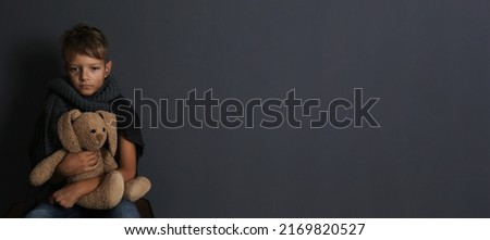 Poor boy sitting with toy rabbit on dark background, space for text. Banner design