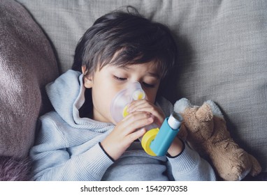 Poor boy tired from chest coughing holding inhaler mask, Child closing his eyes while using the volumtic for breathing treatment,Tried Kid having asthma allergy using the asthma inhaler - Powered by Shutterstock