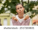 Poor Caucasian young woman holding one dollar banknotes outdoors. Lack of money to buy purchase something in store. Financial crisis. Bankruptcy. Poverty and destitution. Girl on urban city street