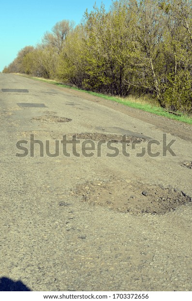 Poor condition of the\
road surface. Spring season. Hole in the asphalt, risk of movement\
by car, bad asphalt, dangerous road, potholes in asphalt.Poltava\
Region. Ukraine