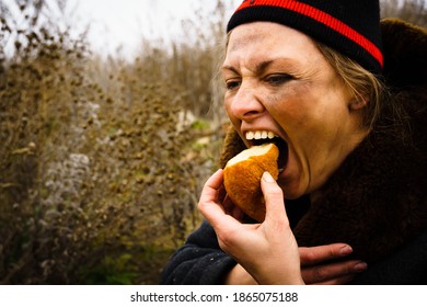 The Poor Dirty Woman Greedily Eats A Piece Of Bread. Hungry Homeless Woman In Outdated Clothes. Free Space For Text