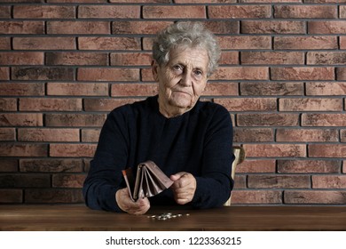 Poor Elderly Woman With Empty Wallet And Coins At Table