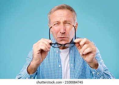 Poor Eyesight. Mature Man Can't See, Squinting Eyes Putting On Glasses Having Problems With Vision, Looking At Camera At Blue Studio. Ophtalmic Issue, Bad Sight In Older Age, Macular Degeneration - Shutterstock ID 2100084745