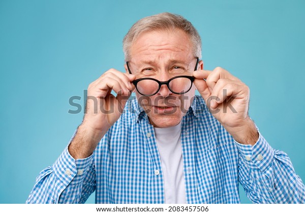 Poor Eyesight. Senior Man Can\'t See, Squinting\
Eyes Wearing Glasses Having Problems With Vision, Looking At Camera\
At Blue Studio. Ophtalmic Issue, Bad Sight In Older Age, Macular\
Degeneration Concept