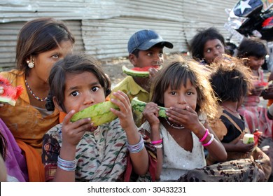 A Poor Girl In India Eating Watermelon Along With Her Other Family Who Spend Their Time Begging On The Streets. Focus On The Eyes Of The Girl In Front.