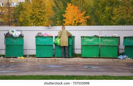 Poor Homeless Old Man Searching In Garbage In Autumn Time. Men Rummaging In Trash Container Looking For Food And Reusable Goods