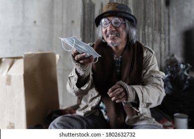 Poor Homeless Old Man Smiling And Holding Face Mask While Sitting In The Corner Of The Building Near The Wall Blur Face