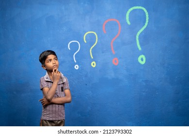 Poor Indian Kid Deep Thinking On Blue Studio Background With Big Growing Question Marks - Concept Of Thoughtful About Future, Wisdom And Poverty.