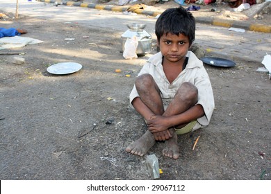 A poor kid in India, sitting on the streetside.