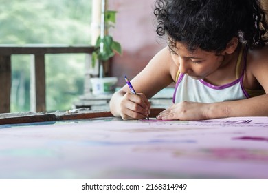 poor latina girl with brown skin very concentrated painting her drawing. disheveled girl with frizzy hair and old clothes doing her homework at a desk next to nature. concept of poverty and humility. - Shutterstock ID 2168314949
