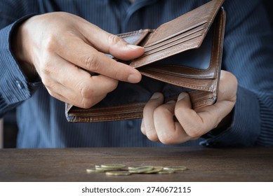 Poor man hands opening empty leather wallet with few coins on wooden table. Financial crisis, debt, and poverty and expenses are insufficient.concept.

