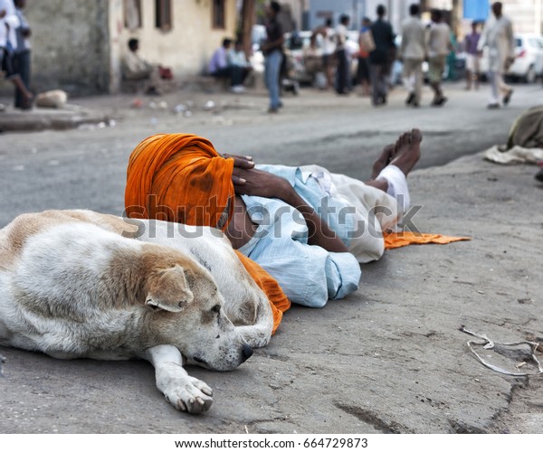 A POOR MAN\
SLEEPING ON A DOG AS PILLOW, NEW DELHI, INDIA - SEPTEMBER 29, 2012:\
A poor man sleeps on the road divider with his head resting on a\
street dog in New Delhi,\
India