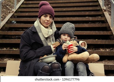 Poor mother and daughter with bread sitting on stairs outdoors