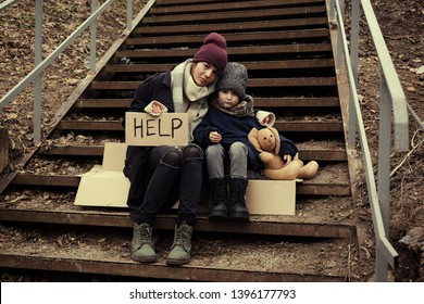 Poor Mother And Daughter With HELP Sign Sitting On Stairs Outdoors