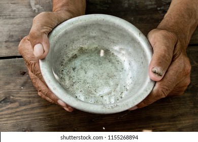 The Poor Old Man's Hands Hold An Empty Bowl Of Beg You For Help. The Concept Of Hunger Or Poverty. Selective Focus. Poverty In Retirement. Alms