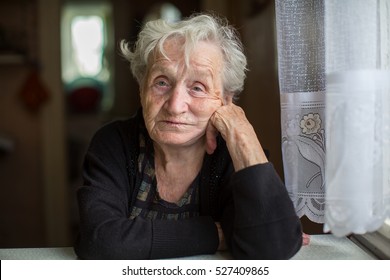 Poor Old Woman In Her Home, Looking Into The Camera.