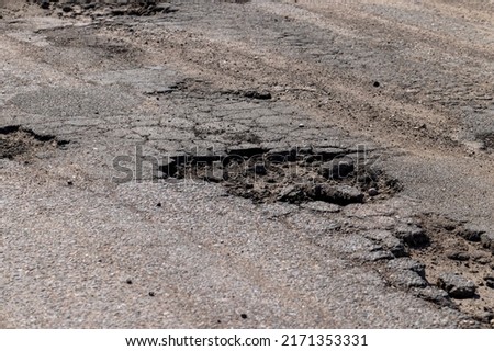 poor paved road with a lot of holes and potholes, poor transport infrastructure with an unrepaired road with a pit and a pothole