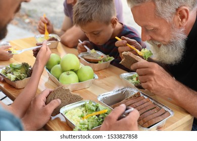 Poor People Eating Food At Wooden Table Outdoors