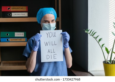 Poor Prediction Or Outlook From Doctor. Sarcastically Smiling Nurse In Protective Uniform Holds A Paper Sheet With The Inscription That Everyone Will Die. Pandemic Concept.