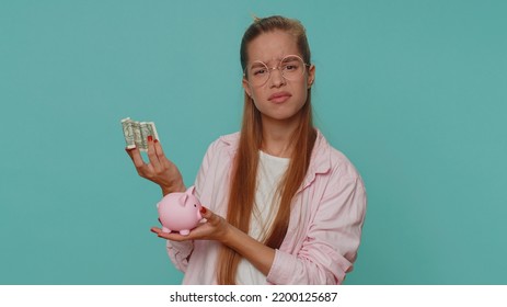 Poor Pretty Teenager Girl Insufficient Amount Of Money, Holding Piggybank And One Dollar Banknote. Financial Crisis. Bankruptcy. Poverty And Destitution. Young Child Kid On Blue Background Indoors