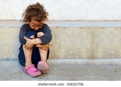 poor, sad little child girl sitting against the concrete wall