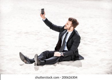 Poor signal. Frustrated young businessman searching for mobile phone signal while sitting on sand in desert