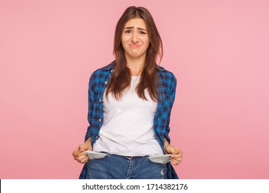Poor student, unemployment. Portrait of upset jobless girl in checkered shirt turning out empty pockets, showing no money gesture, worried about debts. indoor studio shot isolated on pink background