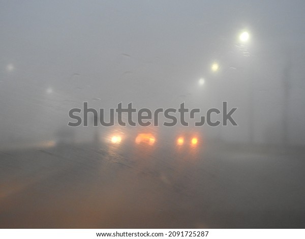 Poor visibility on the road due to heavy mist\
and fog early in the morning on the highway. slow-moving cars in\
heavy smoke and dangerous traffic in bad weather and slippery\
asphalt, blurry background