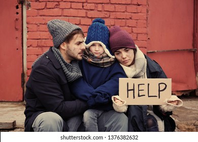 Poor Young Family With HELP Sign On Dirty Street