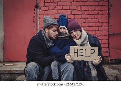 Poor Young Family With HELP Sign On Dirty Street