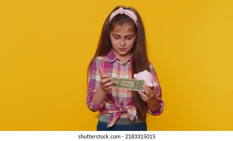 Poor Young Preteen Child Girl Kid Insufficient Amount Of Money, Holding Piggybank And One Dollar Banknote At Home. Financial Crisis. Bankruptcy. Poverty And Destitution. Little Toddler Children Alone