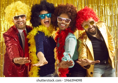 Pop Music Band Singing At Night Club. Young People Disguised In Fancy Feather Boas And Funny Silly Curly Wigs Dancing Together. Happy Multiethnic Men And Women Having Fun At Halloween Disco Party