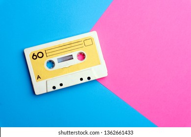 Pop music style attributes eighties, retro old school 80-s or 90-s concept. Audio cassette on a bright blue-pink creative background