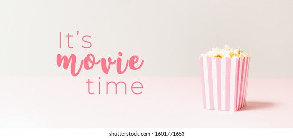 Popcorn Bag With White And Pink Stripes At The Light Neutral Backdrop. Empty Minimalistic Background. Romantic Movie Night And Snack Concept With It's Movie Time Wording. Banner Wide Screen Format