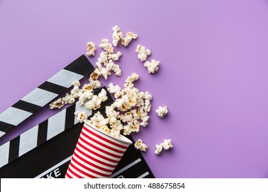 Popcorn and clapperboard on colorful background.