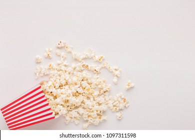 Popcorn In Classic Striped Bucket On White Background. Hot Corn Scattered From Paper Box, Copy Space. Fast Food And Movie Snack