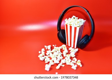 Popcorn in colored cardboard packaging with headphones for listening to music and watching a movie. Heap of salted popcorn in paper striped bucketon a red background. - Powered by Shutterstock