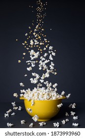 Popcorn falling into a yellow bowl on a black background. Transformation process
