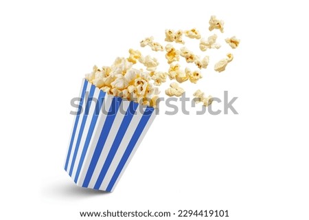 Popcorn flying out of blue white striped paper box isolated on white background with copy space. Splash, levitation of popcorn grains. 