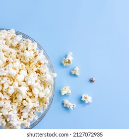 Popcorn in glass bowl on blue background. Top view, square banner. Selective focus, copy space