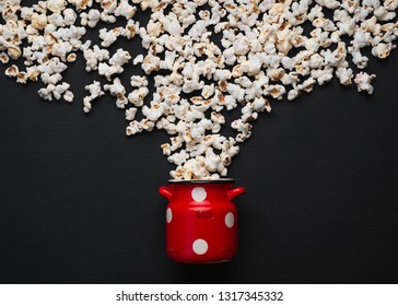 popcorn on a black background, pouring out of a red can with white polka dots - Powered by Shutterstock