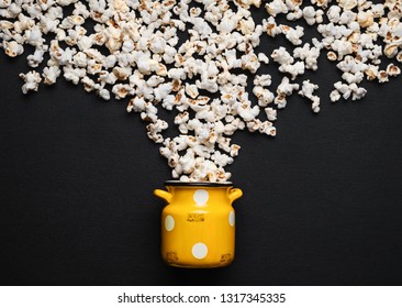 popcorn on a black background, pouring out of a yellow can with white polka dots - Powered by Shutterstock