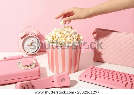 Popcorn in paper cup, devices, alarm clock and hand on pink background