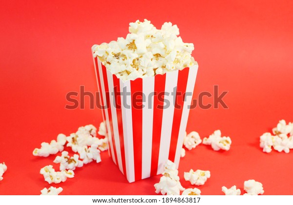 popcorn in paper packaging\
on a red background. Popcorn in red and white packaging. Cinema\
background