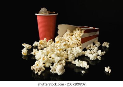 Popcorn in a paper striped box, traditional cardboard bucket and plastic cup of cold cola with ice. Delicious cinema snack and beverage for a film show, movie theater composition on black background. - Powered by Shutterstock