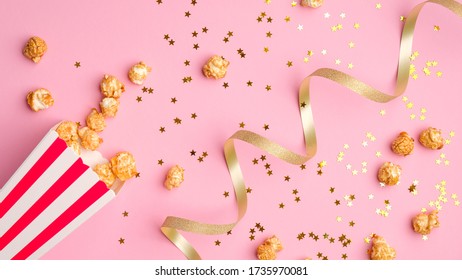 Popcorn in red and white paper bucket scattered on pink background with golden ribbon and confetti. - Powered by Shutterstock