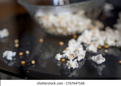 Popcorn spilled all over the table, with a bowl with more popcorn in it visible in the background
