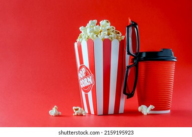 Popcorn In A Striped Cardboard Box, 3d Glasses, A Paper Glass With A Drink On A Red Background, Copy Space. Movie Time.