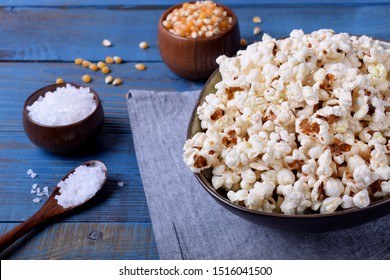 Popcorn, unpopped kernels and sea salt on blue wooden table